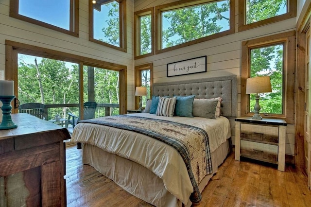 bedroom with wooden walls, light wood-type flooring, and a high ceiling