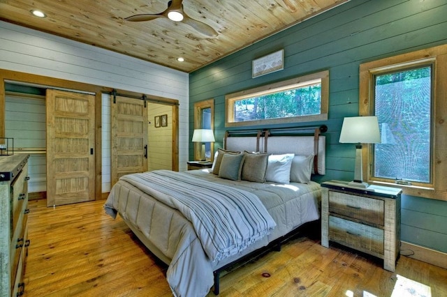 bedroom with wooden ceiling, a barn door, ceiling fan, and light wood-type flooring