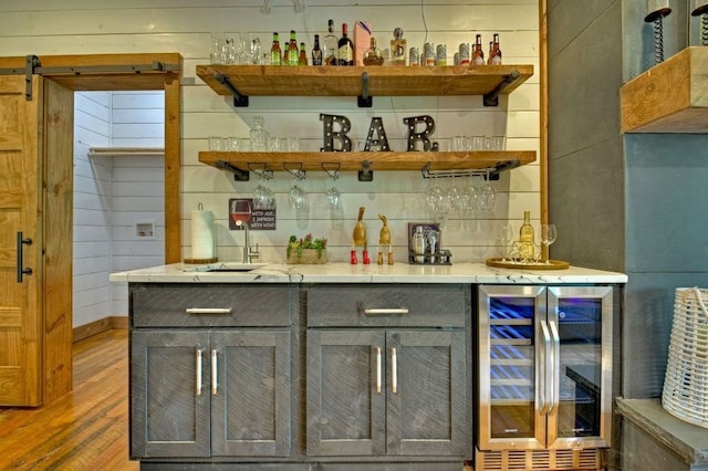 bar featuring gray cabinetry, beverage cooler, and wood walls