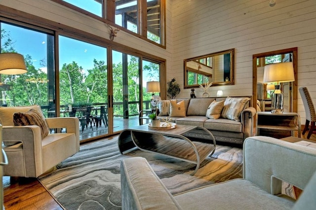 living room featuring a healthy amount of sunlight, wood-type flooring, a towering ceiling, and wooden walls