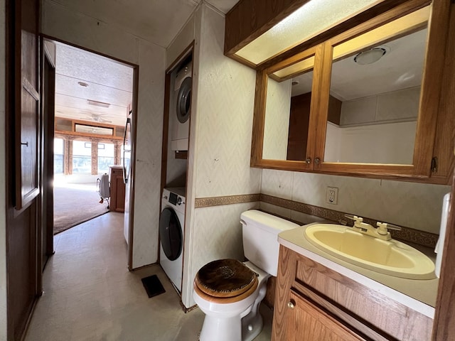 half bathroom featuring tile patterned floors, stacked washer and dryer, vanity, and toilet