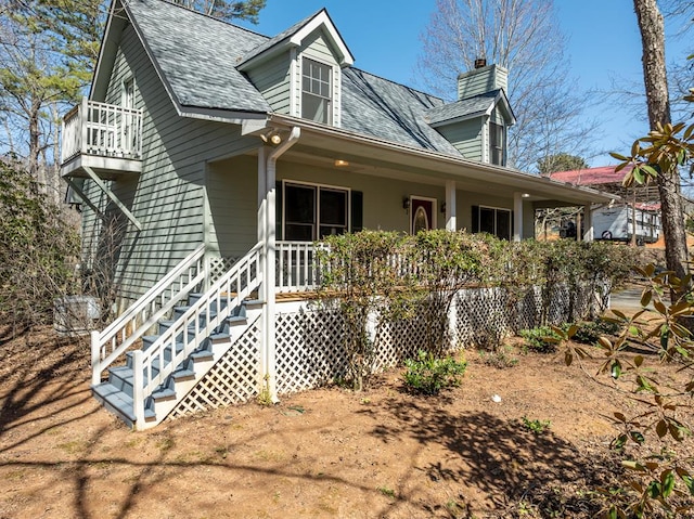 view of front of house with a balcony, a porch, a chimney, and roof with shingles