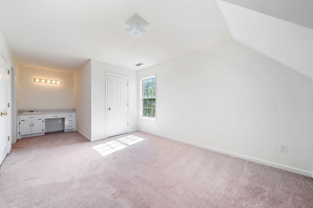 unfurnished bedroom with light carpet, visible vents, baseboards, vaulted ceiling, and a textured ceiling