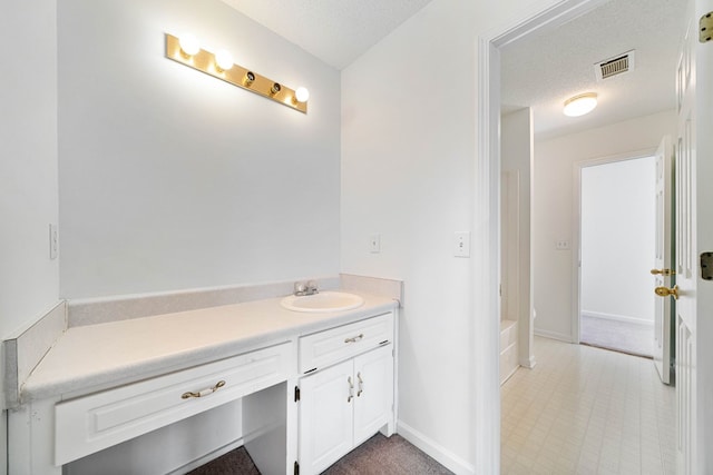 bathroom with a textured ceiling, vanity, visible vents, baseboards, and a bath