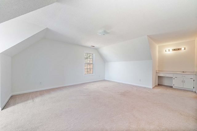 additional living space featuring baseboards, vaulted ceiling, a textured ceiling, and light colored carpet