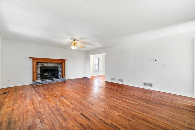 unfurnished living room featuring ceiling fan, visible vents, wood finished floors, and a stone fireplace