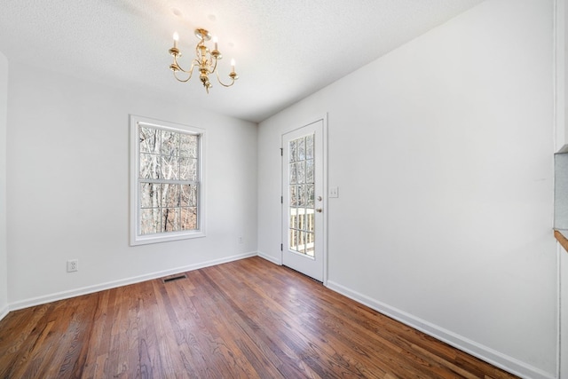 unfurnished dining area with a textured ceiling, a notable chandelier, wood finished floors, visible vents, and baseboards