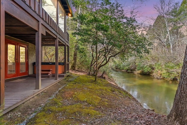 yard at dusk with french doors, a deck with water view, and a hot tub