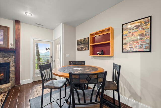 dining area with a stone fireplace and dark wood-type flooring