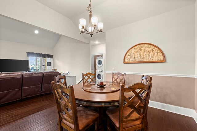 dining space featuring stacked washing maching and dryer, vaulted ceiling, dark wood-type flooring, and an inviting chandelier