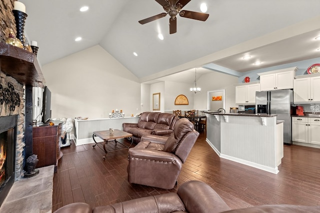 living room featuring ceiling fan with notable chandelier, dark hardwood / wood-style floors, high vaulted ceiling, and a stone fireplace