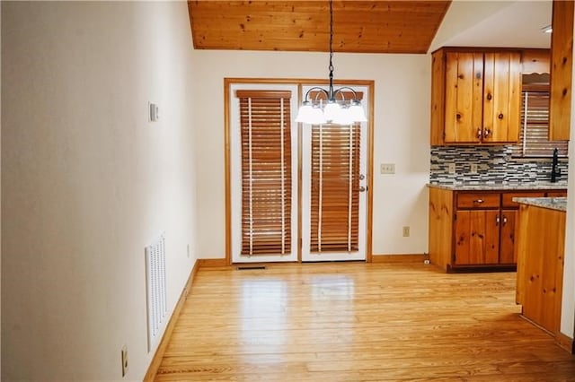 unfurnished dining area with visible vents, lofted ceiling, baseboards, light wood-type flooring, and a notable chandelier