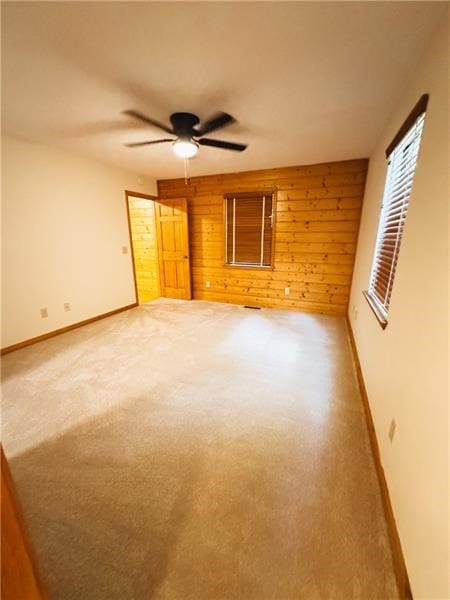 unfurnished room with baseboards, a ceiling fan, wood walls, and carpet flooring