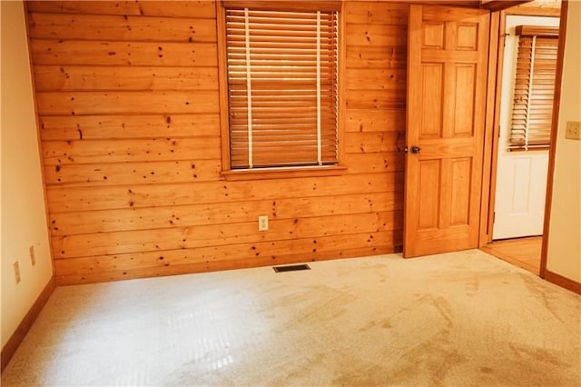 carpeted spare room with wooden walls, baseboards, and visible vents