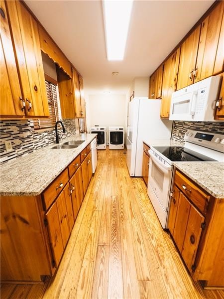 kitchen with a sink, light wood-style flooring, white appliances, and tasteful backsplash