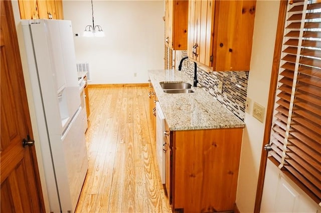 kitchen featuring backsplash, white refrigerator with ice dispenser, brown cabinets, a sink, and light wood-style floors