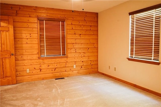 empty room with visible vents, wood walls, carpet, and baseboards
