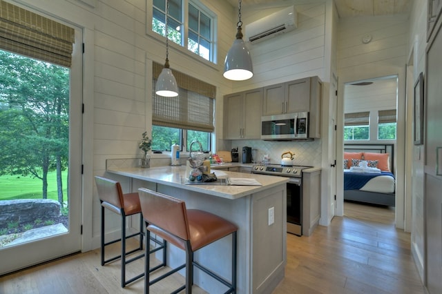 kitchen featuring high vaulted ceiling, wooden walls, a wall mounted AC, decorative light fixtures, and stainless steel appliances