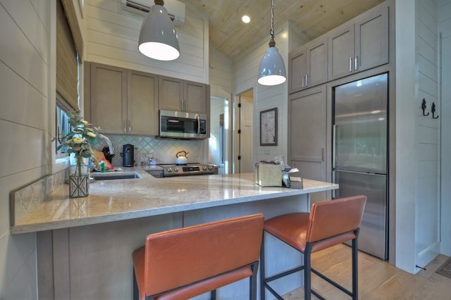 kitchen with kitchen peninsula, light wood-type flooring, stainless steel appliances, vaulted ceiling, and pendant lighting