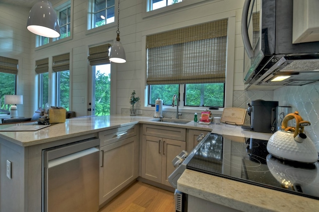 kitchen with hanging light fixtures, light stone counters, plenty of natural light, and sink