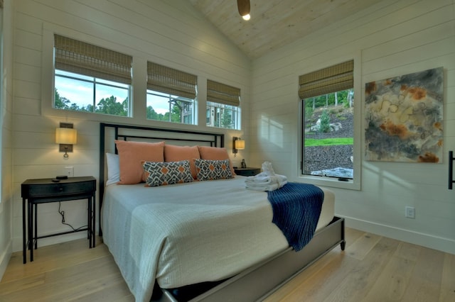 bedroom featuring multiple windows, wooden walls, light hardwood / wood-style flooring, and high vaulted ceiling