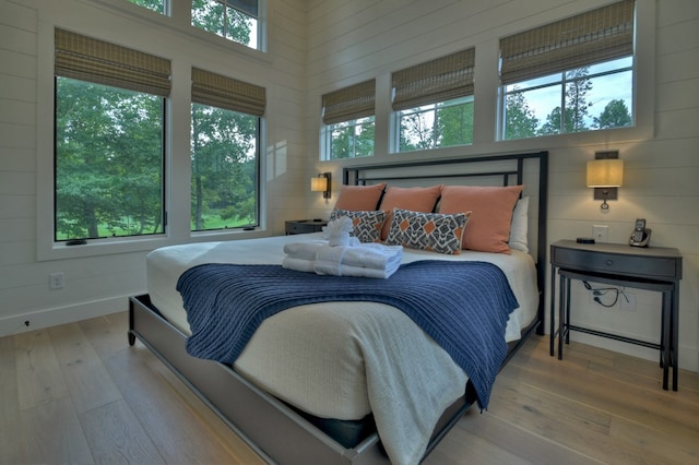 bedroom with light wood-type flooring, a high ceiling, and wooden walls