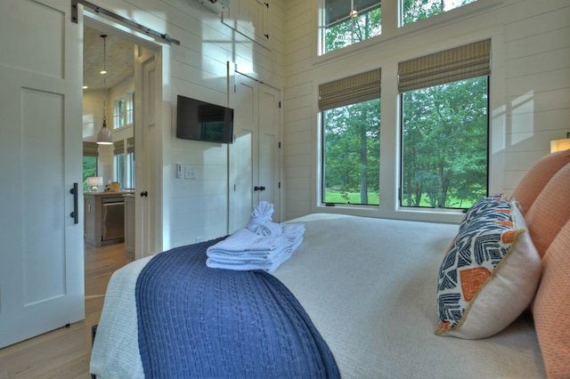 bedroom with a barn door, wooden walls, a towering ceiling, and light hardwood / wood-style floors