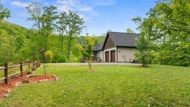 view of yard with a garage, central AC, and a view of trees