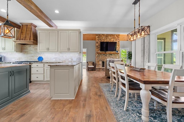 kitchen featuring light wood-style floors, premium range hood, tasteful backsplash, pendant lighting, and beam ceiling
