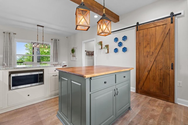 kitchen with stainless steel microwave, light wood-style flooring, wooden counters, beamed ceiling, and pendant lighting