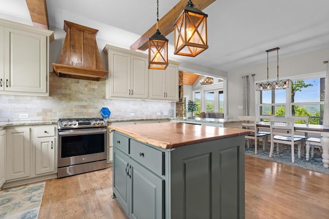 kitchen featuring stainless steel gas range oven, custom range hood, light wood-style floors, backsplash, and a kitchen island