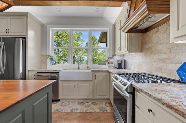 kitchen with appliances with stainless steel finishes, custom exhaust hood, a sink, decorative backsplash, and wooden counters