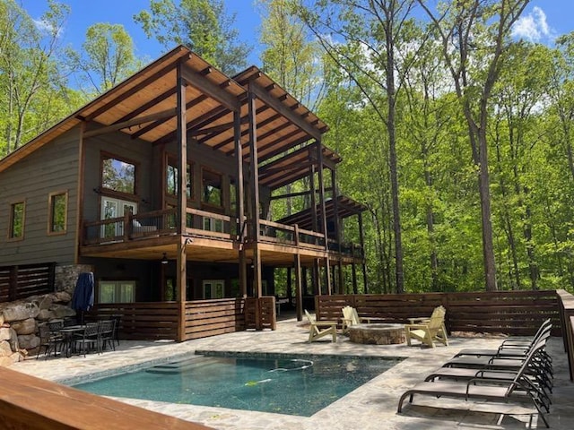 rear view of property with an outdoor pool, a fire pit, a balcony, and a patio