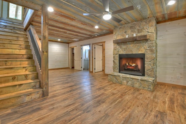 unfurnished living room with wood finished floors, baseboards, a fireplace, stairs, and ceiling fan