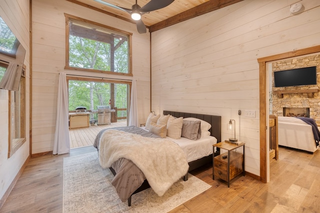 bedroom with light wood finished floors, wooden walls, a towering ceiling, and access to exterior