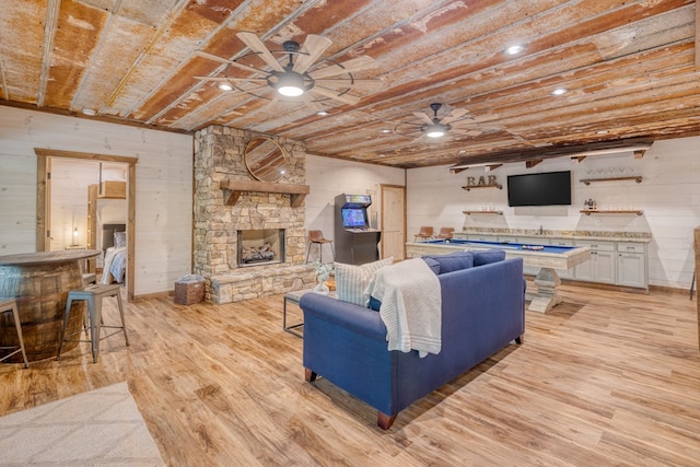 living room featuring ceiling fan, a stone fireplace, wooden walls, and light wood-style flooring