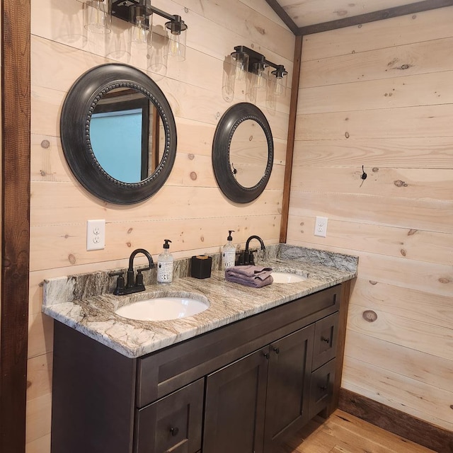 bathroom with wood finished floors, wood walls, a sink, and double vanity
