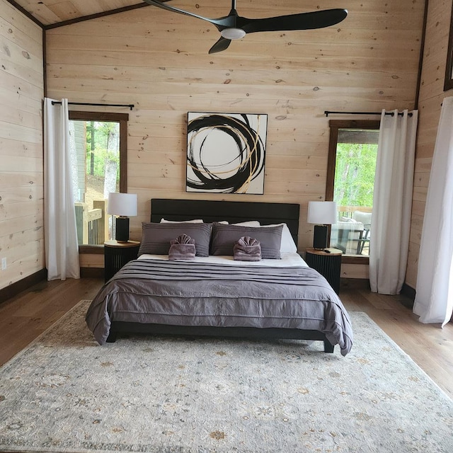 bedroom featuring vaulted ceiling, wood finished floors, wood walls, and multiple windows