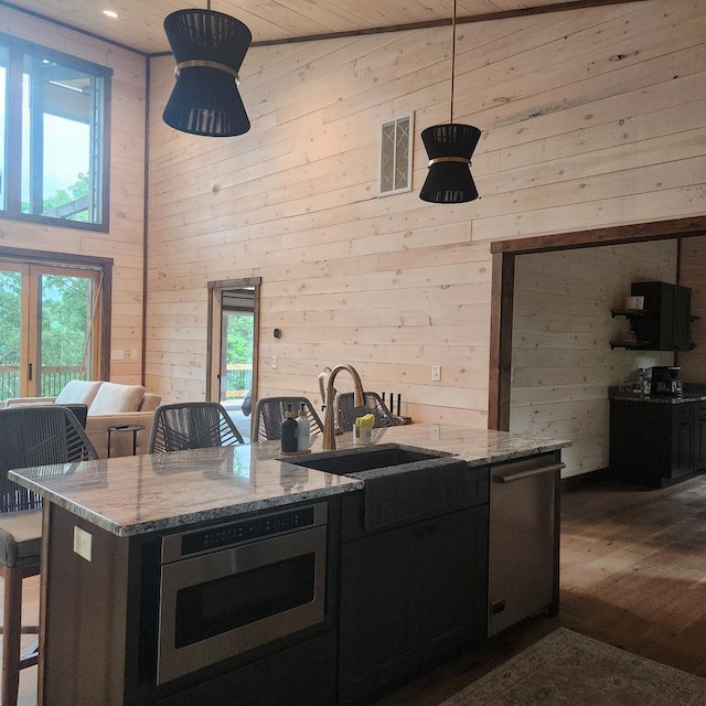 kitchen with a sink, oven, wooden walls, dishwasher, and a high ceiling