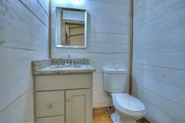 bathroom featuring wood finished floors, wooden walls, vanity, and toilet