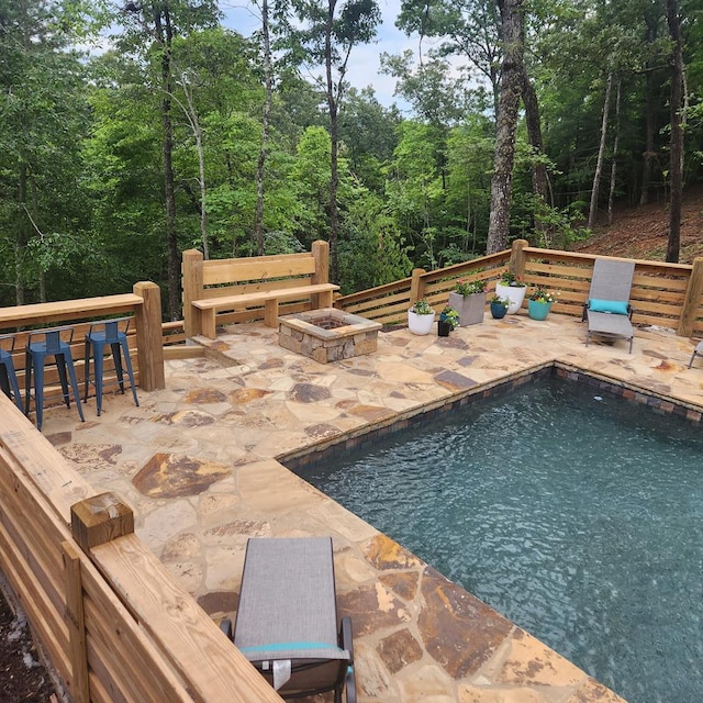 outdoor pool featuring a patio area, a fire pit, and a view of trees
