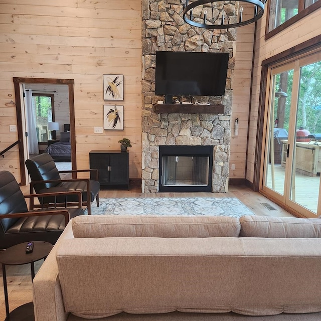 living room with visible vents, wooden walls, wood finished floors, and a stone fireplace