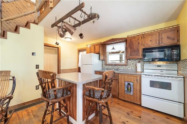 kitchen with white appliances, backsplash, a breakfast bar area, and light wood finished floors