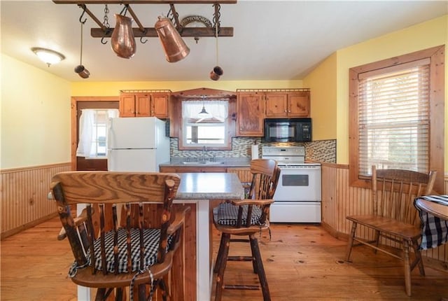 kitchen with a wainscoted wall, light wood-type flooring, brown cabinetry, white appliances, and a sink