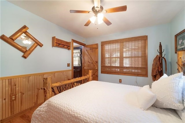 bedroom with a wainscoted wall, wood walls, ceiling fan, and wood finished floors