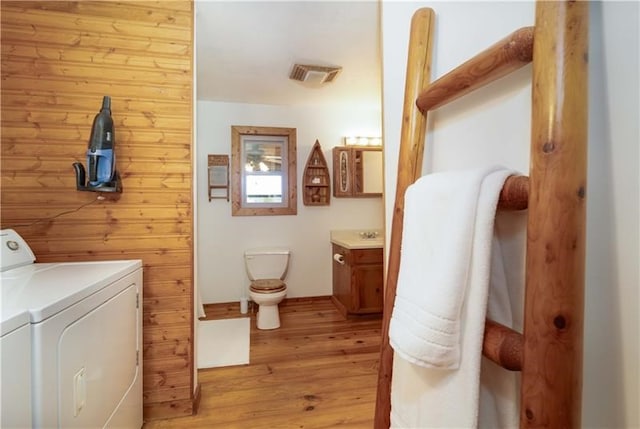 bathroom featuring visible vents, toilet, wood finished floors, separate washer and dryer, and wooden walls