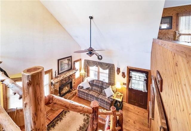 living area featuring a wealth of natural light, high vaulted ceiling, a stone fireplace, and wood finished floors