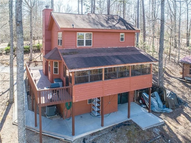 back of property with cooling unit, dirt driveway, a chimney, and a shingled roof