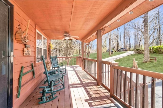 wooden terrace featuring a porch, a ceiling fan, and a lawn