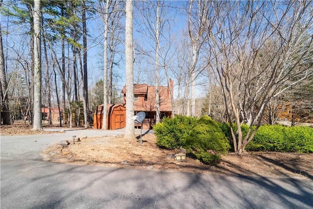 exterior space with an outbuilding, a shed, driveway, and a chimney